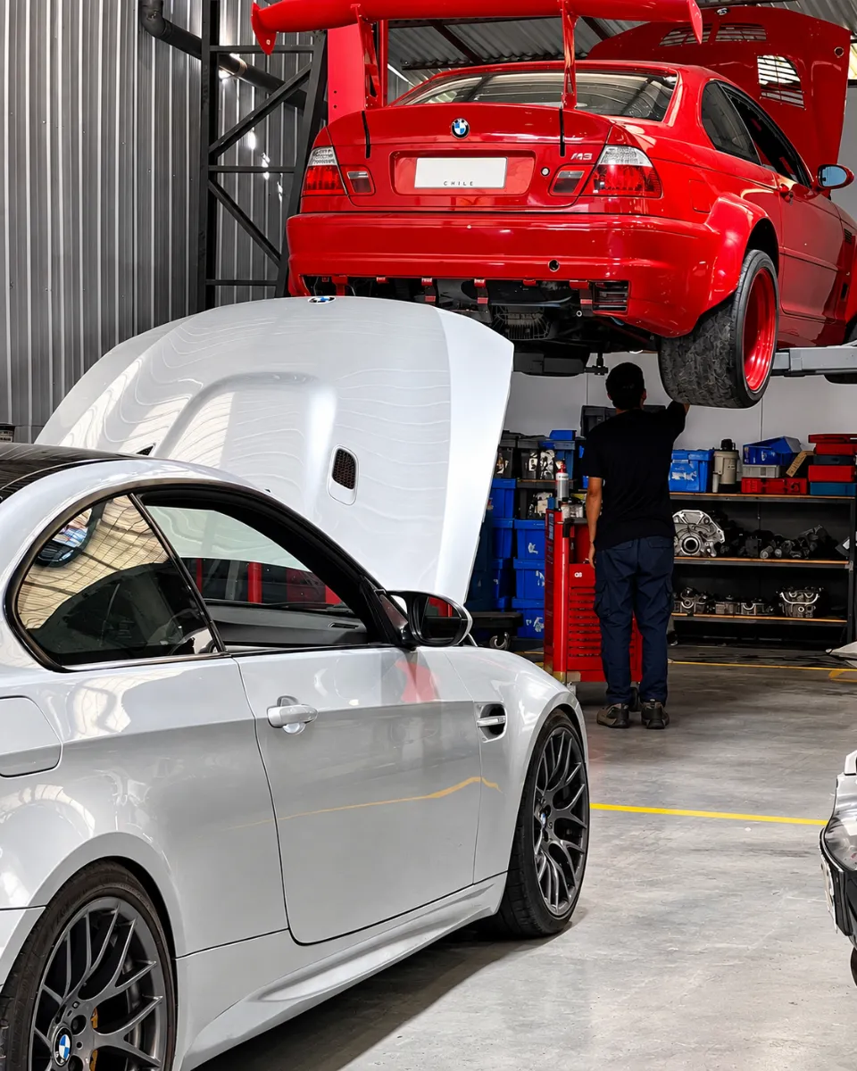 Mecánico revisando un BMW M3 rojo en el elevador junto a un BMW M3 plateado con el capó abierto